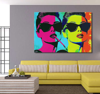 Andy Warhol signature - Audrey Hepburn pop art painting, featuring two stylized portraits, hangs above a yellow sectional sofa with a striped ottoman in a modern living room.