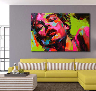Françoise Nielly-signature Colorful Lady painting featuring a vibrant woman's face on a light gray wall, paired with a yellow sofa and striped ottoman in a modern living room.