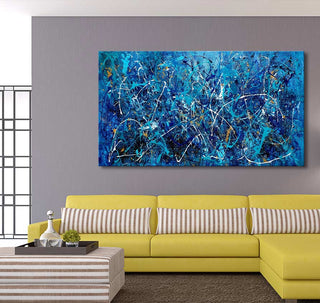 Jackson Pollock signature – The Big Blue: Abstract splatter painting in modern living room with mustard-yellow sectional and striped ottoman. Hand-painted, UV-protected canvas.