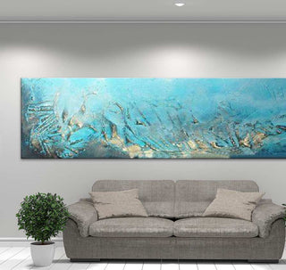 Abstract schilderij 'Big Blue' met dikke olieverf op canvas, in aqua en goudtinten. Hangt boven een lichtgrijze bank, verlicht door plafondspot.