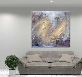 ‘Smokey Gold’ schilderij met abstracte goudbruine kleurschakeringen, dik met paletmes op canvas aangebracht. Hangt boven een grijze bank in een stijlvolle woonkamer.