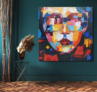 Joseph Lee's 'Woman with Glasses' painting, featuring a colorful abstract face on teal wall, accompanied by a black side table with pampas in a vase.