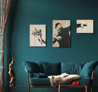 Banksy - The Riot (3-piece): A triptych featuring a stencil-style figure throwing flowers, set against a teal living room with a cozy, modern aesthetic.